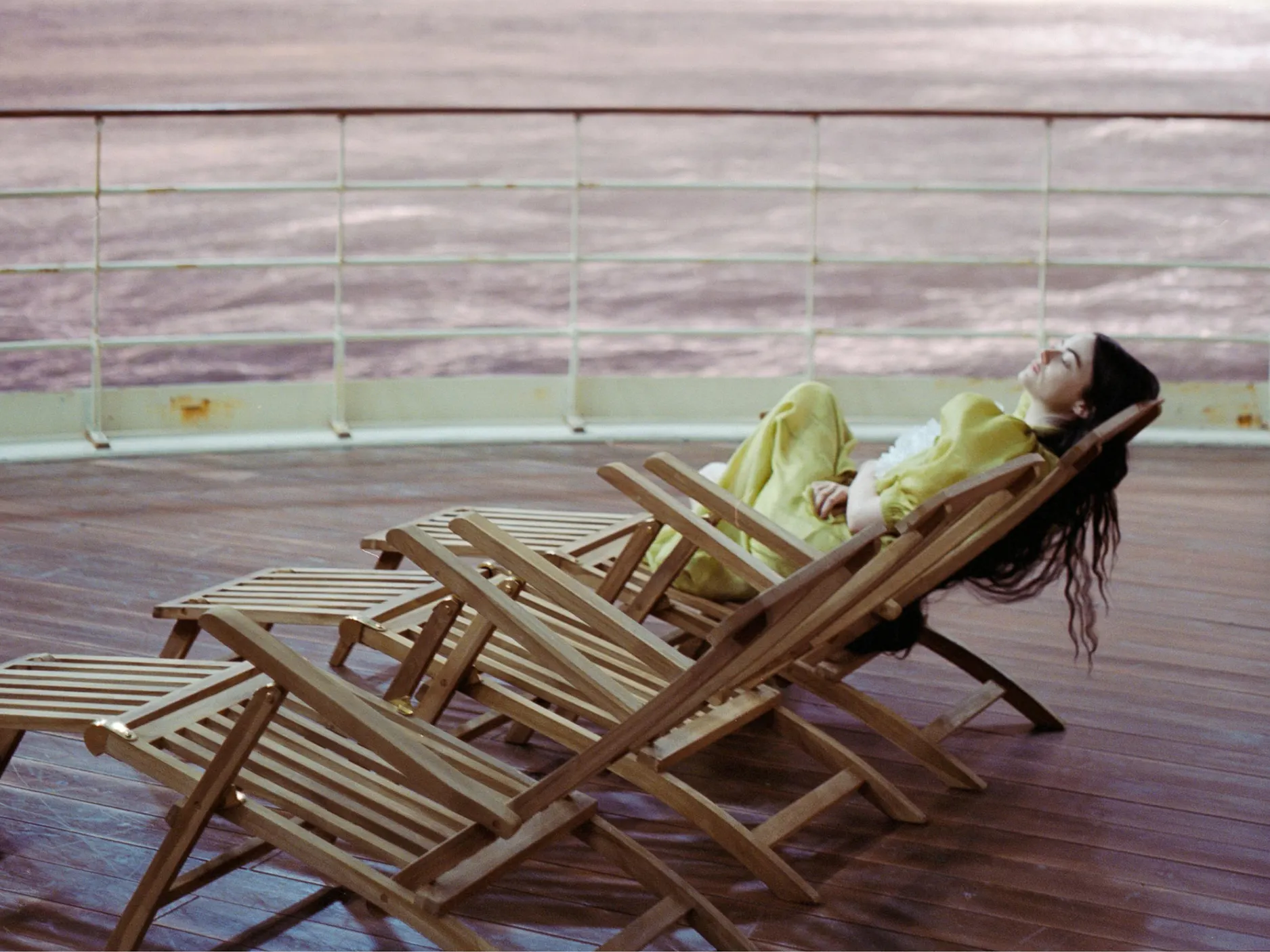 Kader iz filma Nesrečna bitja - ženska v rumeni obleki leži na ležalniku na ladji